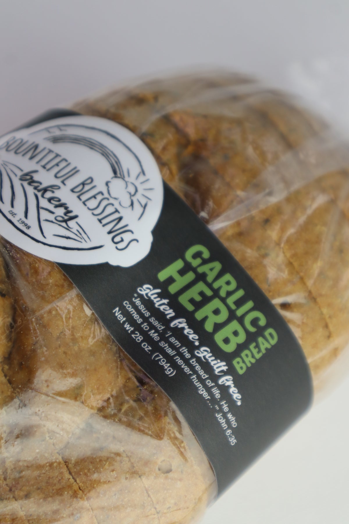 A close-up of a packaged loaf of garlic herb bread from Countenful Blessings Bakery, wrapped in clear plastic with a black and green paper label.