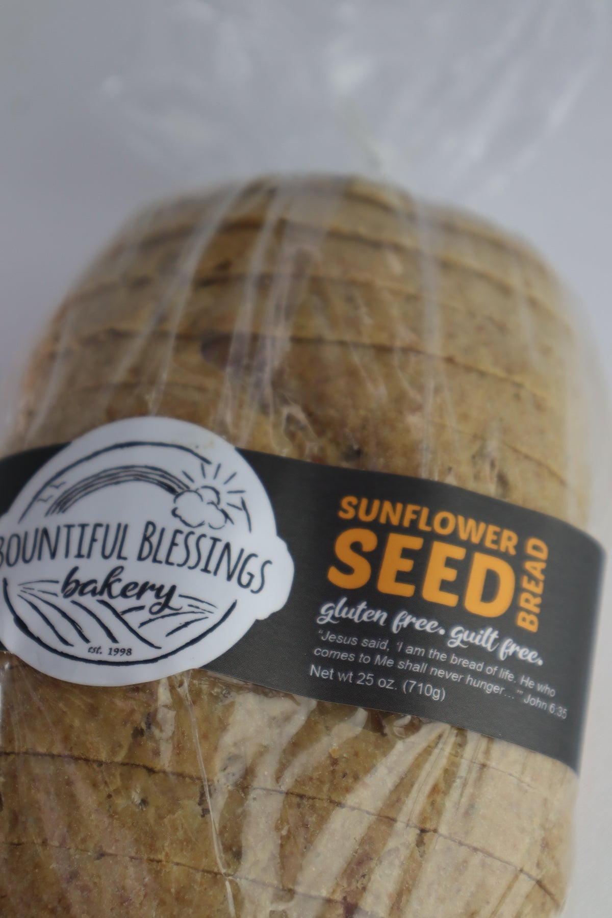 A loaf of sunflower seed bread wrapped in clear plastic with a black and white label from Bountiful Blessings Bakery.